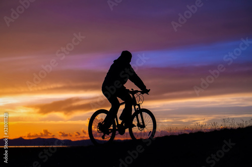 A cyclist rides in the mountains in the evening at sunset. Silhouette raider on a background of magnificent sunset