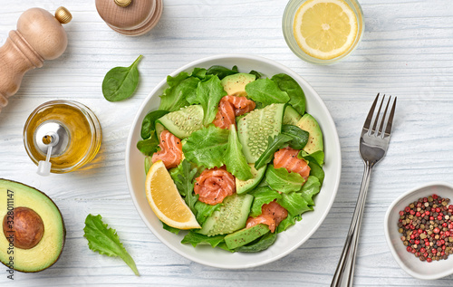 Salmon salad with cucumber, spinach, lollo, lettuce on dish. Healthy seafood, salmon fish, creative diet concept. Tasty salmon and mixed greens vegetarian salad on white wood, top view, flat lay