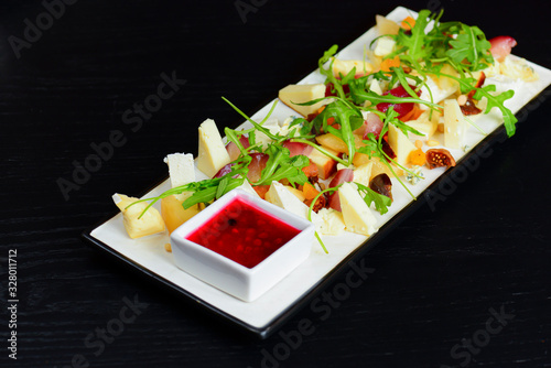 Organic spring mix salad with sifferent kinds of cheese on a white rectangular plate with sauce on wooden table. photo