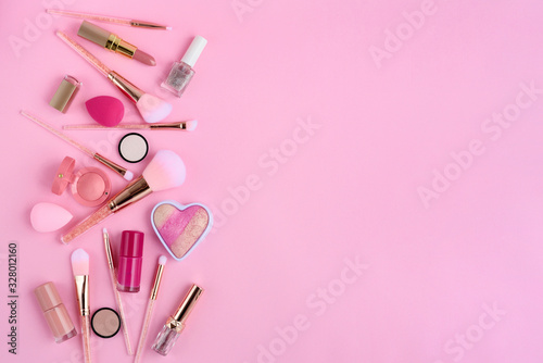 Makeup brushes and decorative cosmetics on pink background, with empty space for text. Top view