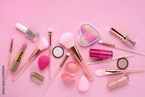 Makeup brushes and decorative cosmetics on a pink background. Top view