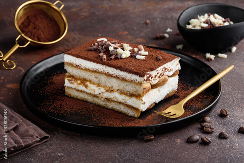 Tiramisu dessert decorated with cocoa and white and dark chocolate on a black plate. Selective focus photo