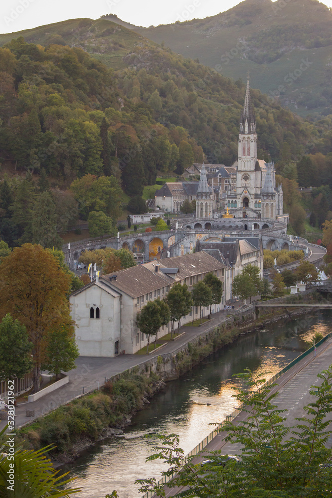 Lourdes landmark in the evening haze filtered. Cathedral of Our Lady of Lourdes with river and mountains. Famous pilgrimage centre. Rosary and sanctuary in Lourdes, France. Religious architecture.