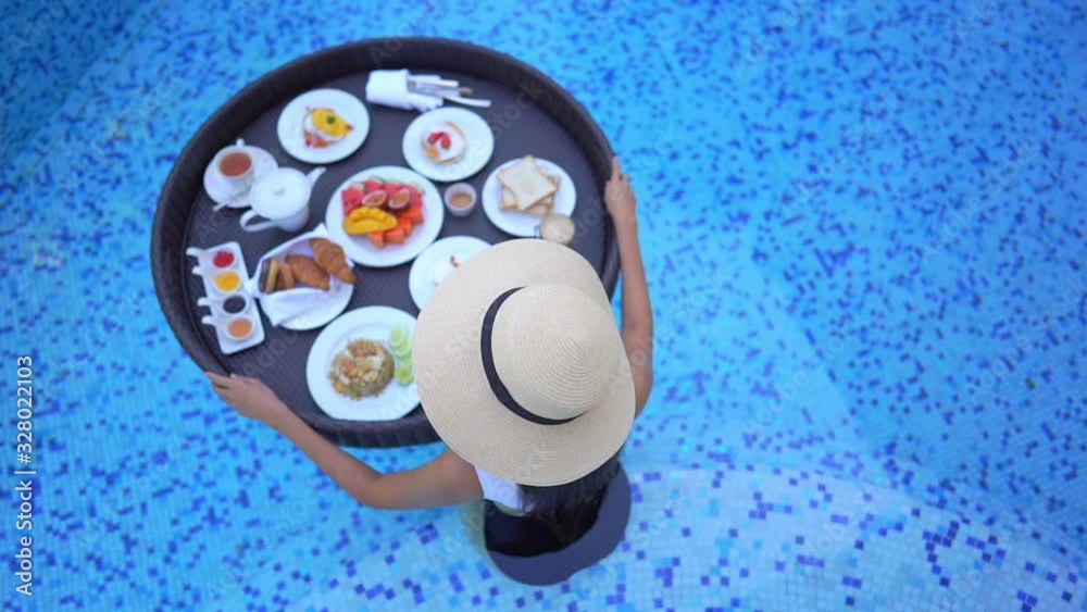Top view of Fit woman holding floating exotic breakfast tray full of fruits and bread, desserts and drinks in swimming pool in the hotel resort. Top view of Fit woman holding floating exotic breakfast tray full of fruits and bread, desserts and drinks in swimming pool in the hotel resort.