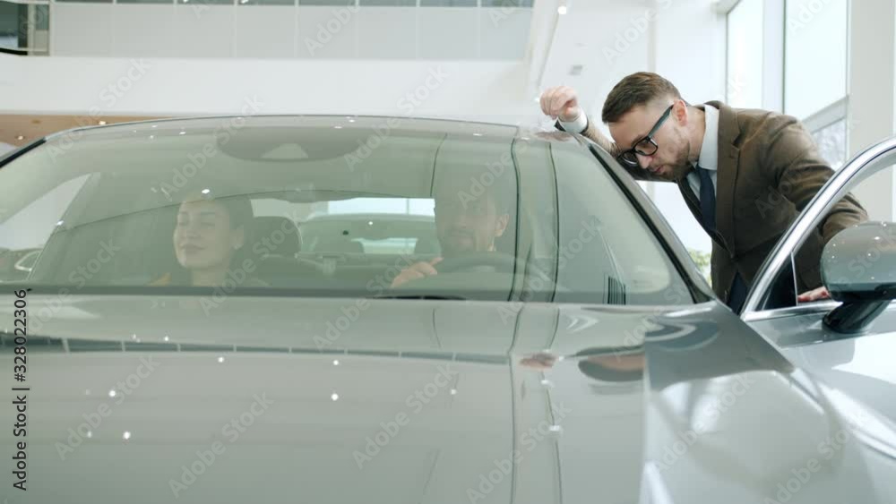 Professional car dealer is talking to young couple buying automobile in dealership describing new model. Profession, business and people concept. Professional car dealer is talking to young couple buying automobile in dealership describing new model. Profession, business and people concept.