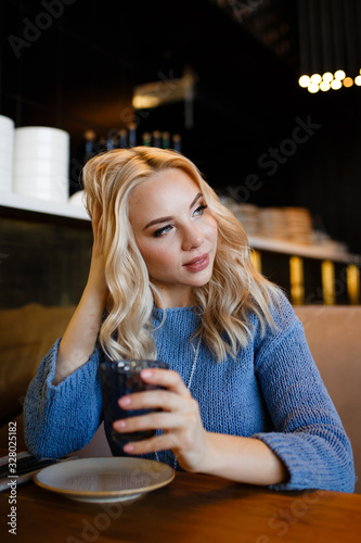 Business portrait of an attractive beautiful blonde woman in a blue jacket and white trousers in a cafe restaurant, a girl working , drinking coffee, talking on the phone, freelancing