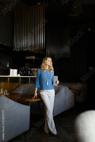 Business portrait of an attractive beautiful blonde woman in a blue jacket and white trousers in a cafe restaurant, a girl working , drinking coffee, talking on the phone, freelancing