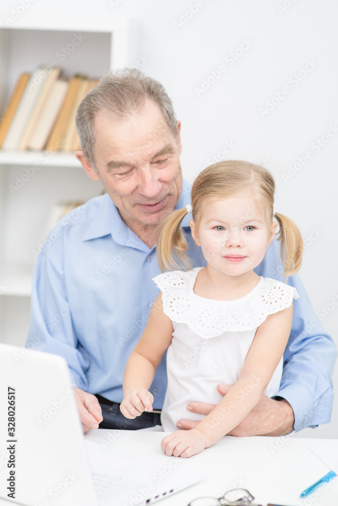 Happy little girl hugging smiling grandfather sitting with laptop