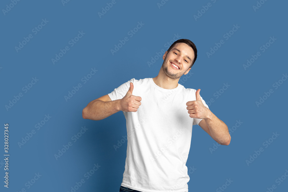 Thumbs up. Caucasian young man's portrait isolated on blue studio background. Beautiful male model in casual style, pastel colors. Concept of human emotions, facial expression, sales, ad. Thumbs up. Caucasian young man's portrait isolated on blue studio background. Beautiful male model in casual style, pastel colors. Concept of human emotions, facial expression, sales, ad.