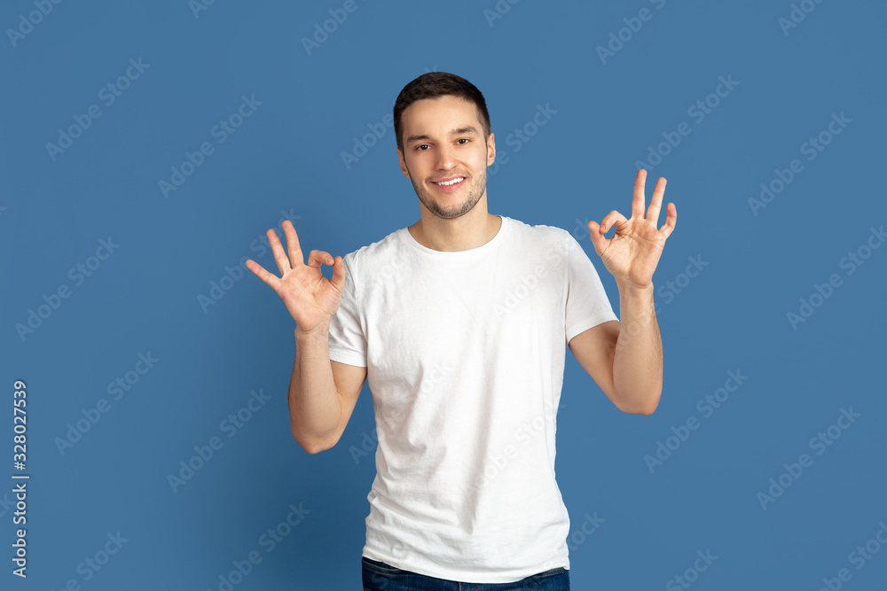 Showing nice. Caucasian young man's portrait isolated on blue studio background. Beautiful male model in casual style, pastel colors. Concept of human emotions, facial expression, sales, ad. Showing nice. Caucasian young man's portrait isolated on blue studio background. Beautiful male model in casual style, pastel colors. Concept of human emotions, facial expression, sales, ad.