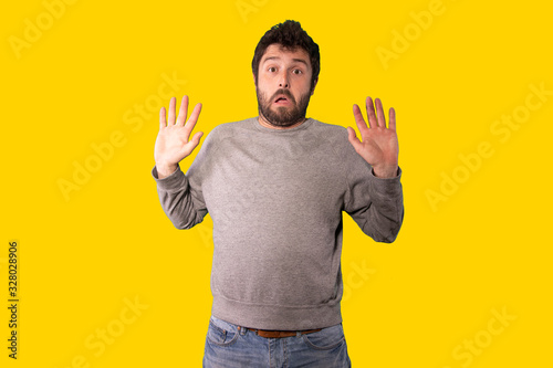 young handsome man feeling stupefied and scared, fearing something frightening, over yellow background. photo