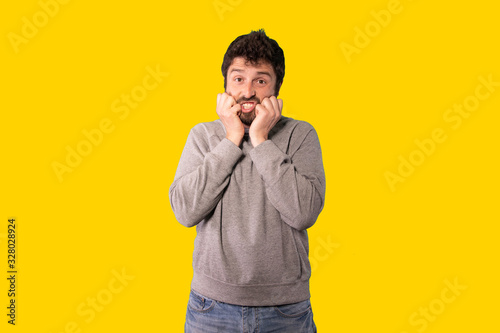 young handsome man feeling stupefied and scared, fearing something frightening, over yellow background.