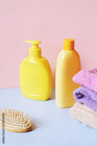 Yellow liquid soap package, orange shampoo bottle, cotton towels and wooden hair brush. Vertical beauty photography