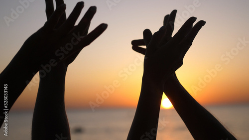 Happy family raising hands up. Hands up in the air silhouette over sunset sky.