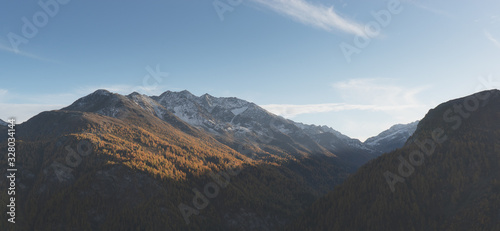 Panoramic quiet Alpine landscape with view of mountain valley and snowy peaks and colorful autumn forest. Background for site or for bunner mood. Enjoy the scenery serene mountains in the evening. © Olya