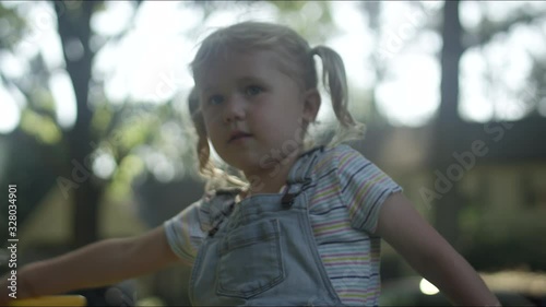 A cute little blonde girl waves a bubble wand and picks her nose in the yard photo