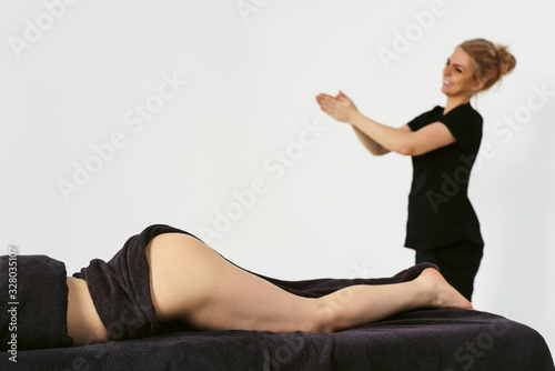 Preparing to massage. Portrait of young smiling friendly cheerful woman masseur in uniforme near massage table with woman patient in wellness center