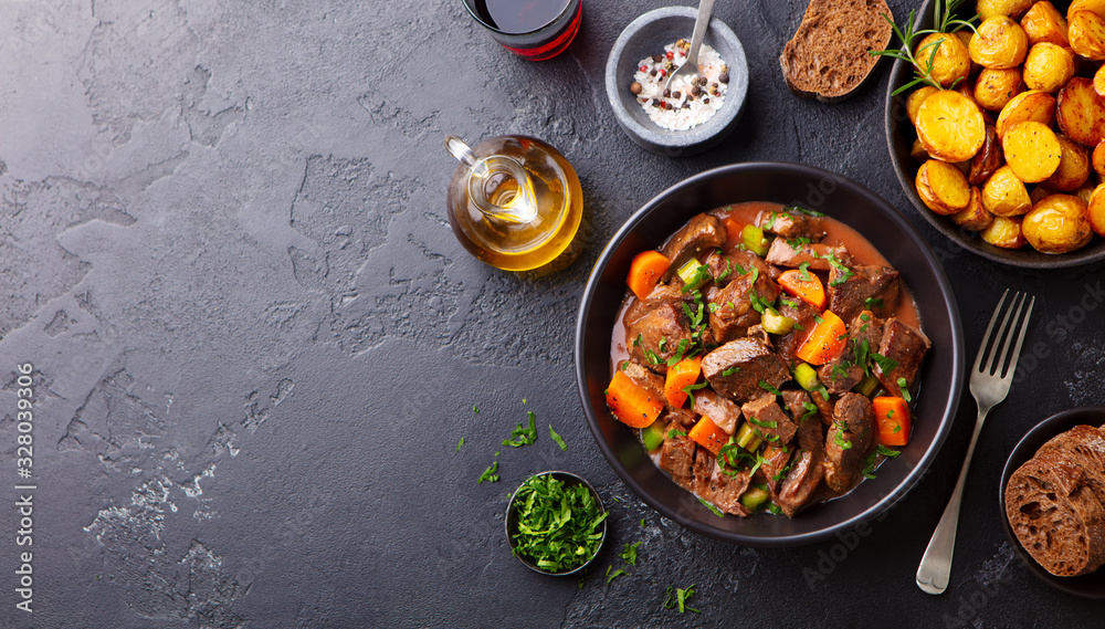 Beef meat and vegetables stew in black bowl with roasted baby potatoes. Dark background. Copy space. Top view. Beef meat and vegetables stew in black bowl with roasted baby potatoes. Dark background. Copy space. Top view.
