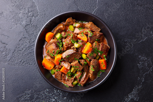 Beef meat and vegetables stew in black bowl. Slate background. Top view.