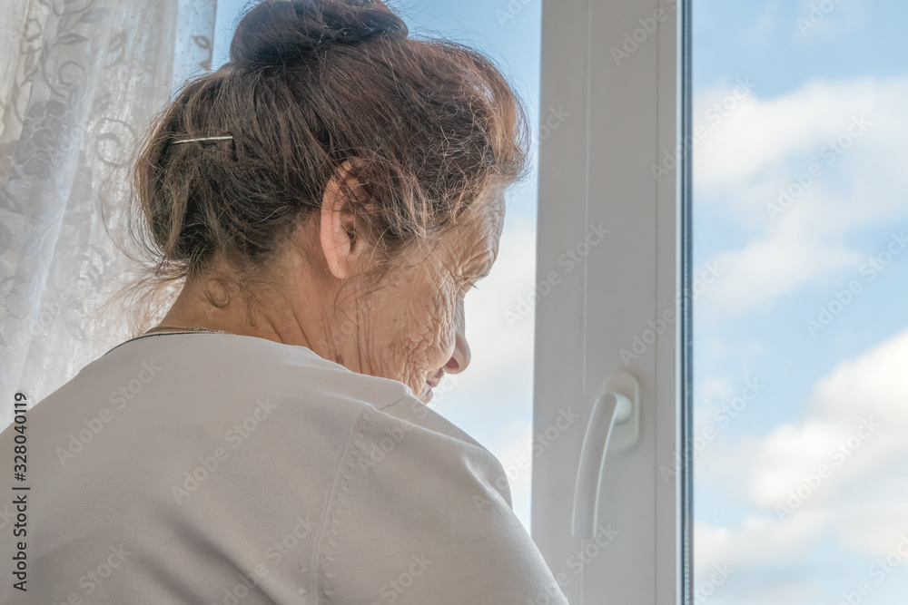 Fototapeta premium elderly dark haired woman stands with her back to the camera by the window