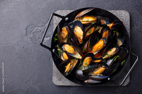 Mussels with herbs and sauce in black pan. Dark background. Copy space. Top view.