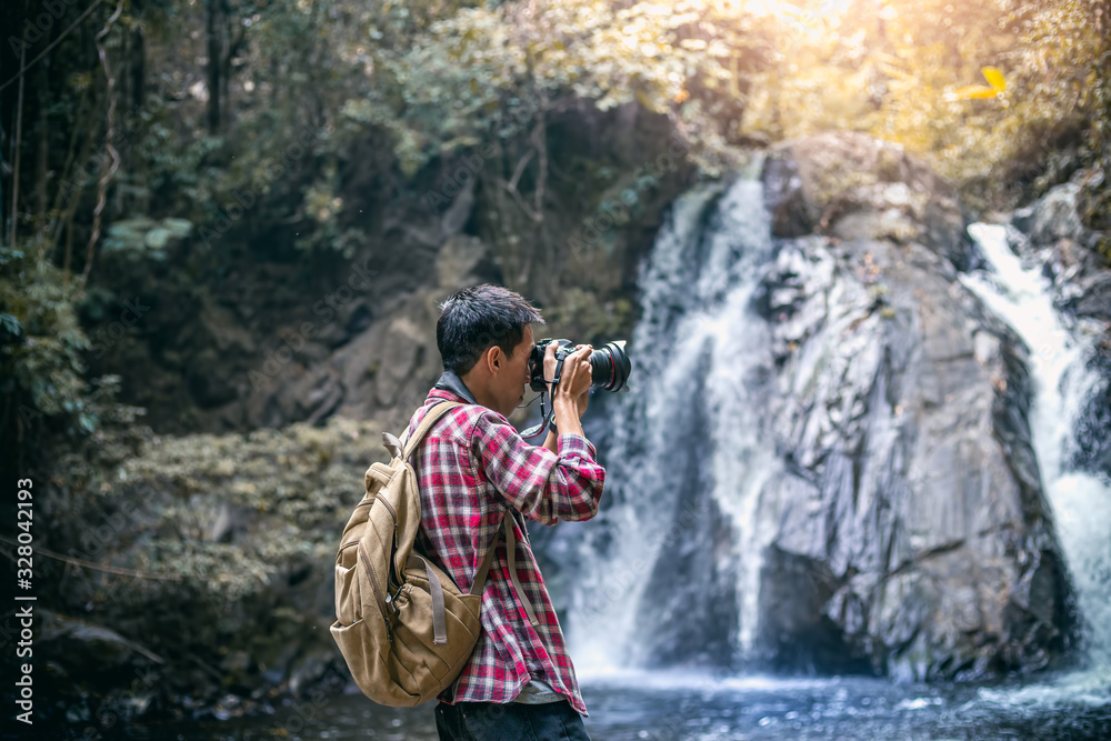 Tourists man or photographer in backpacks standing and holding a camera for taking a photo nature in forest. Tourists man or photographer in backpacks standing and holding a camera for taking a photo nature in forest.