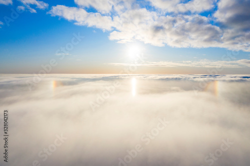Aerial view White clouds in blue sky with solar halo. Top view. View from drone. Aerial bird's eye view. Aerial top view cloudscape. Texture of clouds. View from above. Sunrise or sunset over clouds