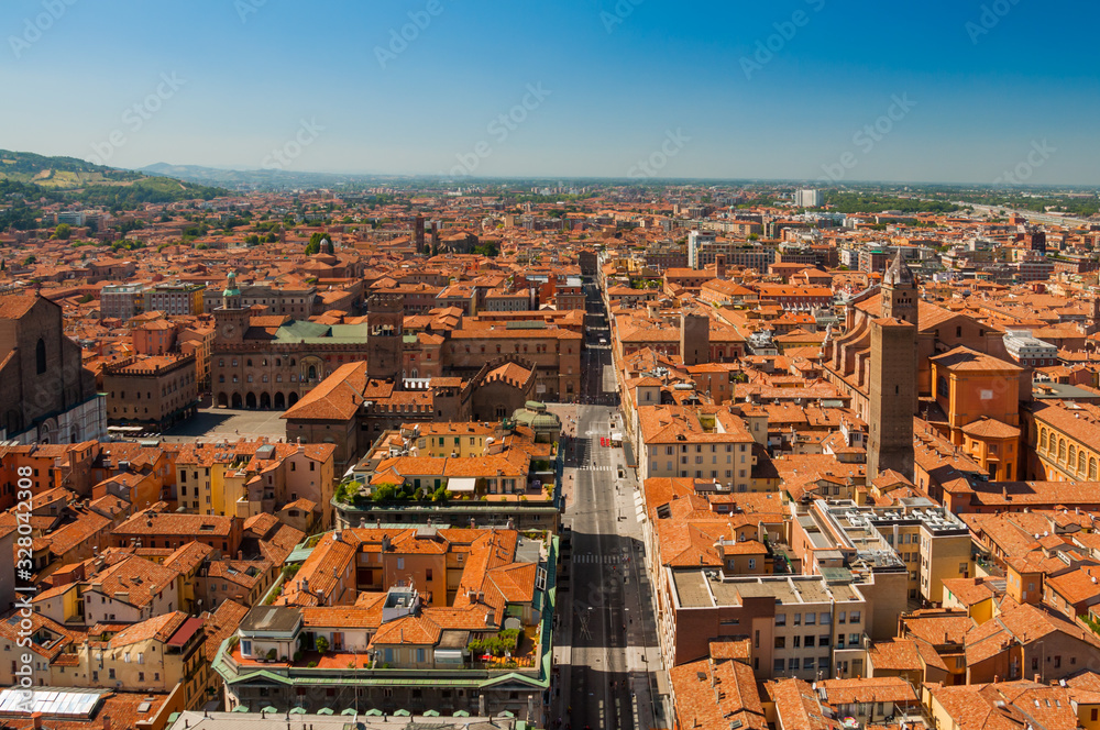 Fototapeta premium Panoramic aerial view of the old Bologna city, with terracotta houses and regular roofs with central square Piazza Maggiore and main street with blue sky over horizon.
