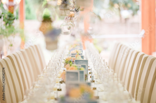 Long dinner tables, served with porcelain and glasses and rich decorated with flowers stand on the roof of a house. Bokeh lights on baclground