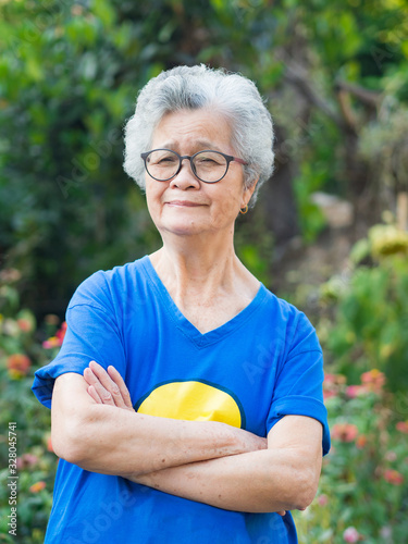 Elderly woman with short white hair standing smiling and arm crossed in the garden. Asian senior woman healthy and have positive thoughts on life make her happy every day. Health concept