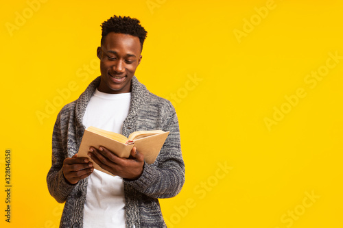 Romantic african guy reading poetry in old book on yellow photo