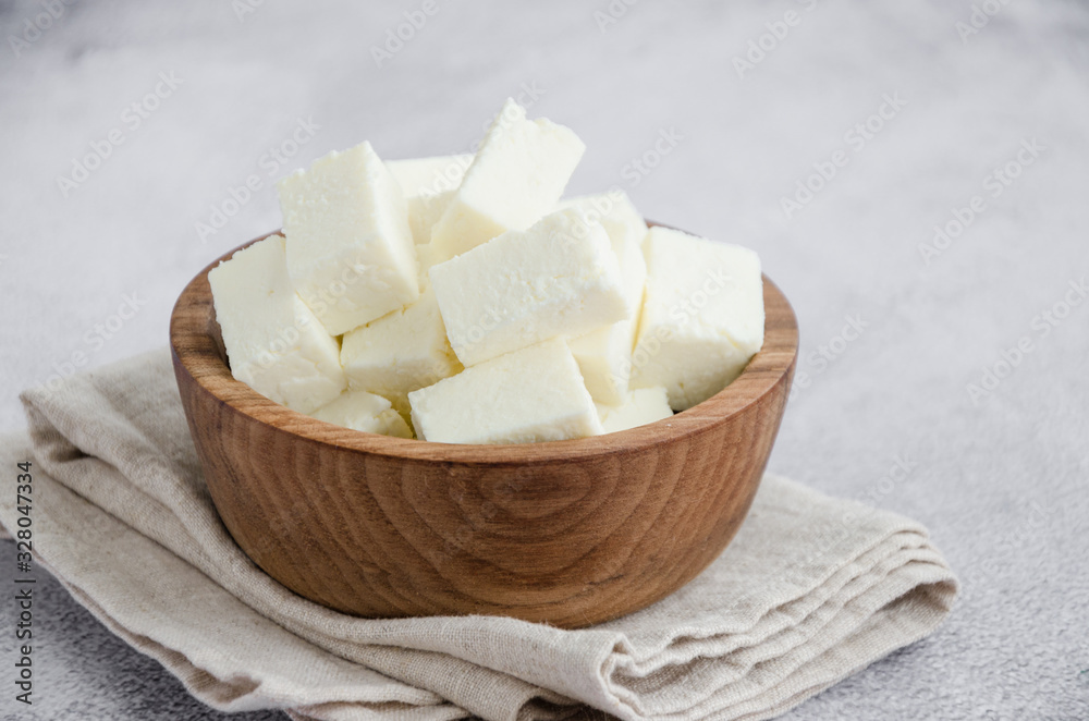 Homemade Indian paneer cheese made from fresh milk and lemon juice, diced in a wooden bowl on a gray stone background. Horizontal orientation. Close up. Homemade Indian paneer cheese made from fresh milk and lemon juice, diced in a wooden bowl on a gray stone background. Horizontal orientation. Close up.