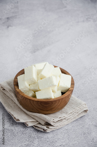 Homemade Indian paneer cheese made from fresh milk and lemon juice, diced in a wooden bowl on a gray stone background. Vertical orientation. Copy space. photo