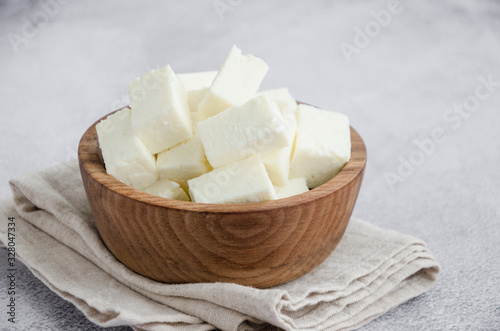 Homemade Indian paneer cheese made from fresh milk and lemon juice, diced in a wooden bowl on a gray stone background. Horizontal orientation. Close up. photo