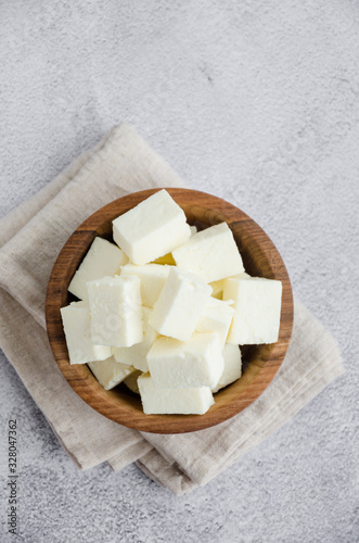 Homemade Indian paneer cheese made from fresh milk and lemon juice, diced in a wooden bowl on a gray stone background. Vertical orientation. Top view. photo