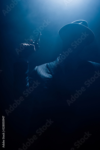 Silhouette of gangster in suit and felt hat with gun on dark background