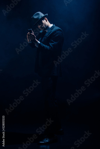 Gangster with clenched hands aiming weapon on dark blue background