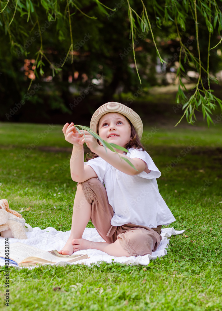 Preschooler girl in a straw hat in the park with book. Child in the park on a summer picnic. Preschooler girl in a straw hat in the park with book. Child in the park on a summer picnic.