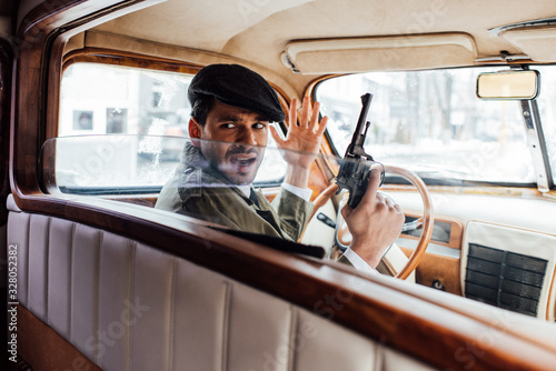 Selective focus of irritated gangster with gun looking back in car