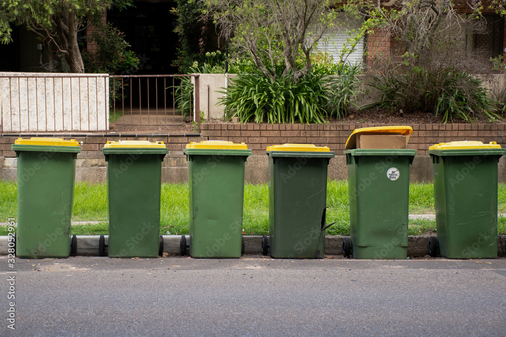 Australian garbage wheelie bins with yellow lids for recycling household waste lined up on the street kerbside for council rubbish collection. Australian garbage wheelie bins with yellow lids for recycling household waste lined up on the street kerbside for council rubbish collection.