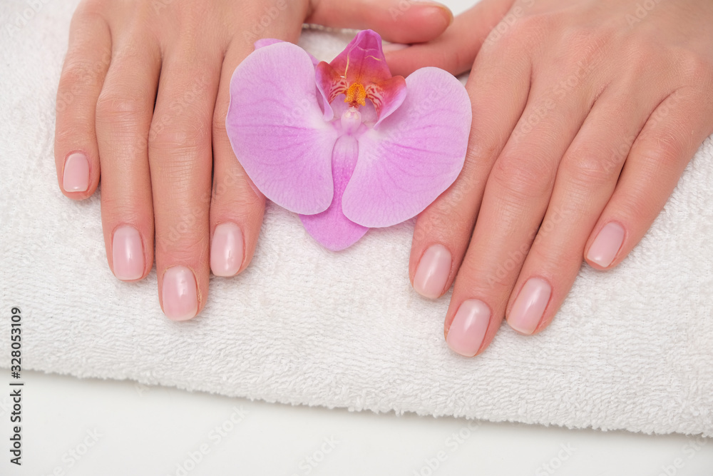 Beuatiful delicate manicure on female hands. The picture of hands lying on the white towel with purple orchid.
