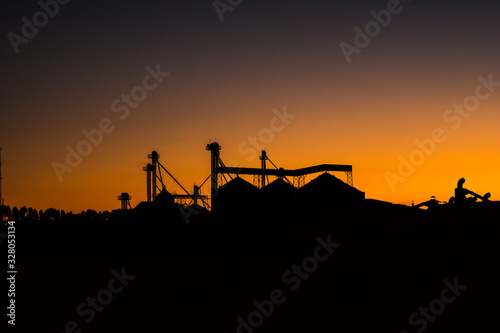 Agriculture - "Golden hour" The sun sets over the silhouette of a soy shed in the early evening. - agribusiness.