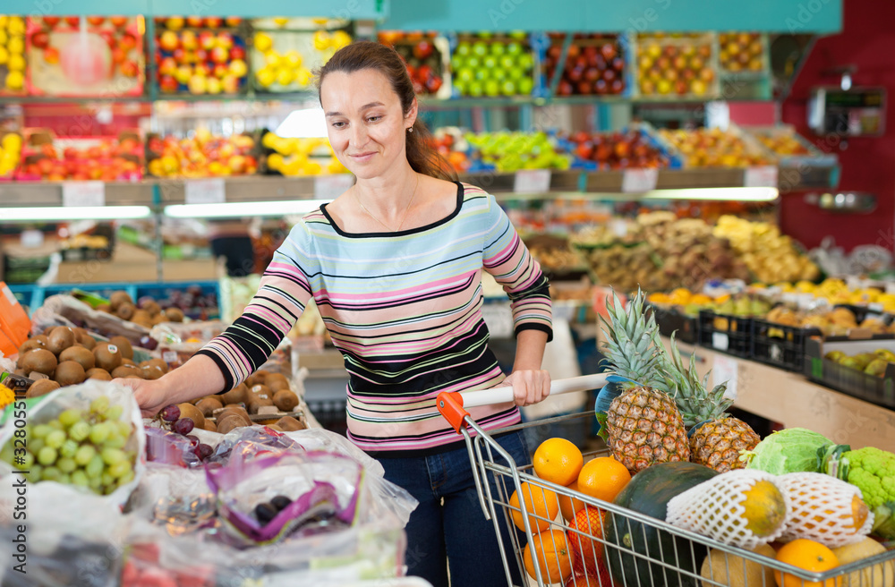 Positive Caucasian female choosing fresh fruits at shop