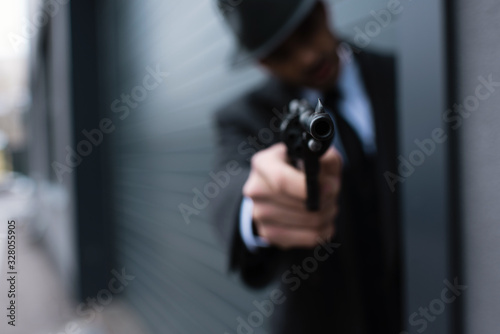 Selective focus of mafioso silhouette with outstretched hand aiming weapon from corner on street