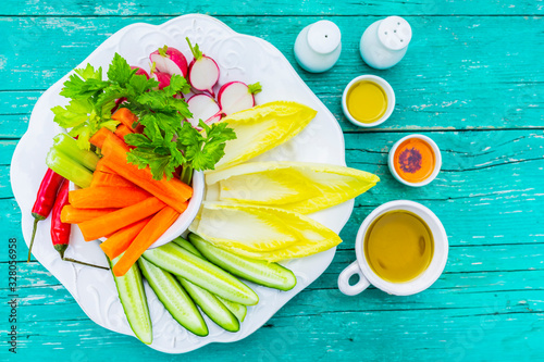 Fresh raw vegetables with different sauces on a white plate and a wooden background. photo