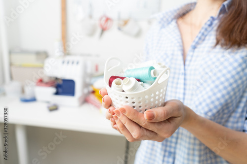 Sewing: a girl holds in her hands a small white basket with spools of thread. photo