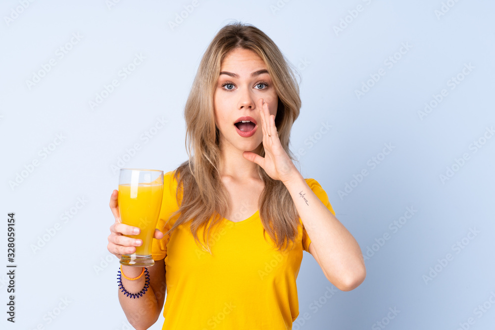 Teenager Russian girl holding an orange juice isolated on blue background shouting with mouth wide open Teenager Russian girl holding an orange juice isolated on blue background shouting with mouth wide open