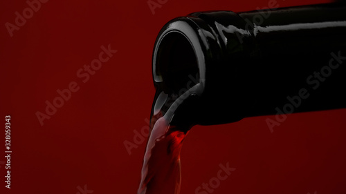 pouring red wine from bottle into wine glass, closeup. red background