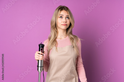 Teenager Russian girl using hand blender isolated on purple background and looking up