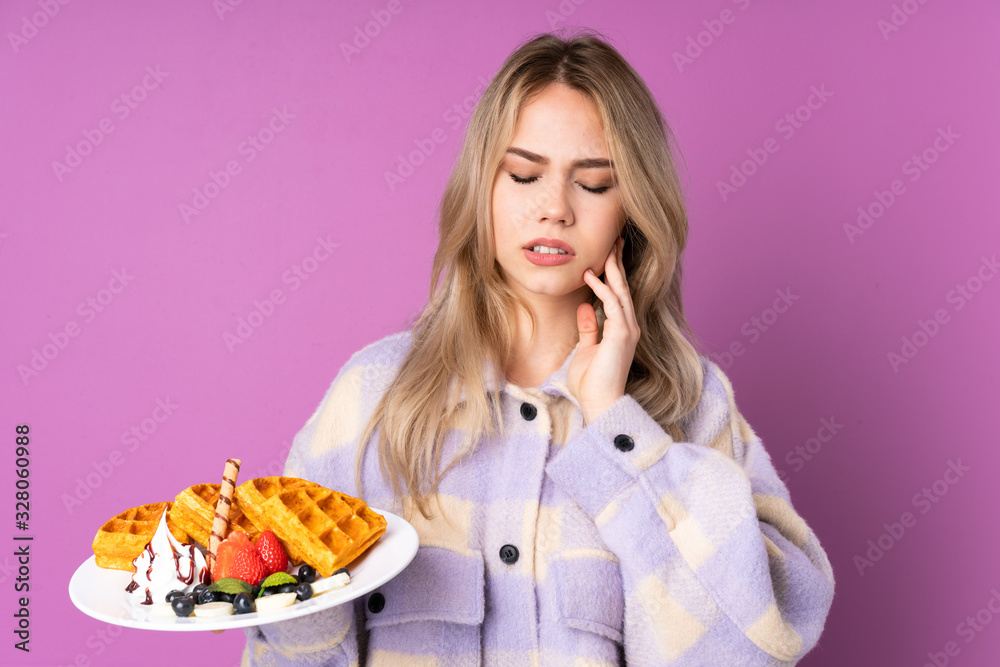 Teenager Russian girl holding waffles isolated on purple background with toothache Teenager Russian girl holding waffles isolated on purple background with toothache